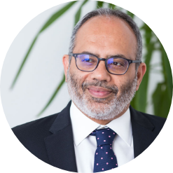 professor Carlos Lopes wearing black-rimmed glasses and a navy blue tie with subtle pink pattern